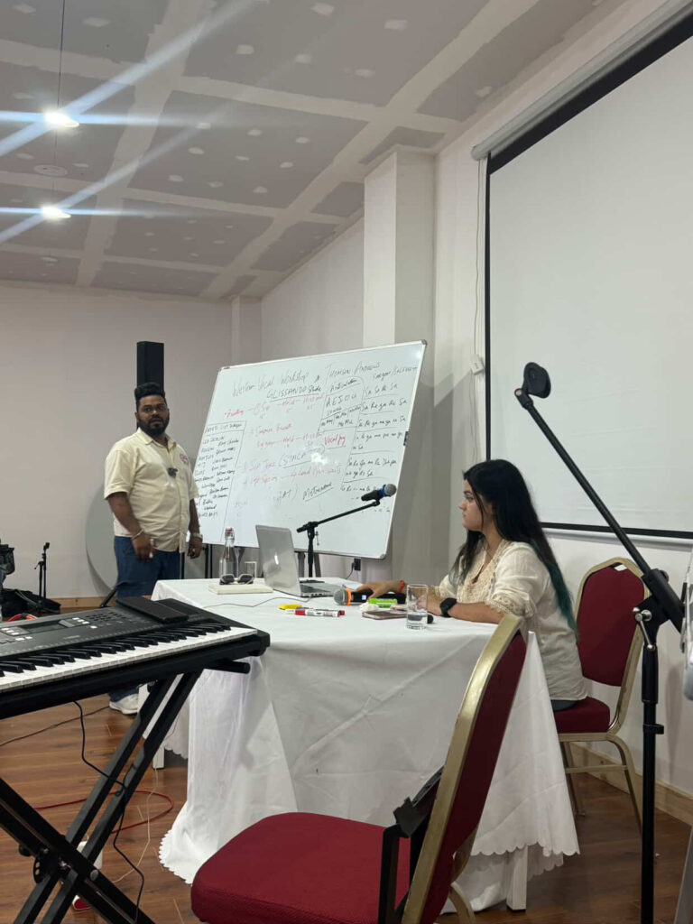 Trainer explains vocal techniques on a whiteboard while another facilitator takes notes during the ongoing workshop in Punakha.