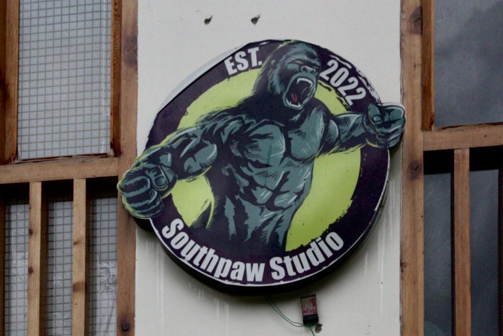 A circular signboard for SouthpawStudio, establishing2022, featuring an muscular gorilla with arms outstreched and mouth open, set against a yellow background.