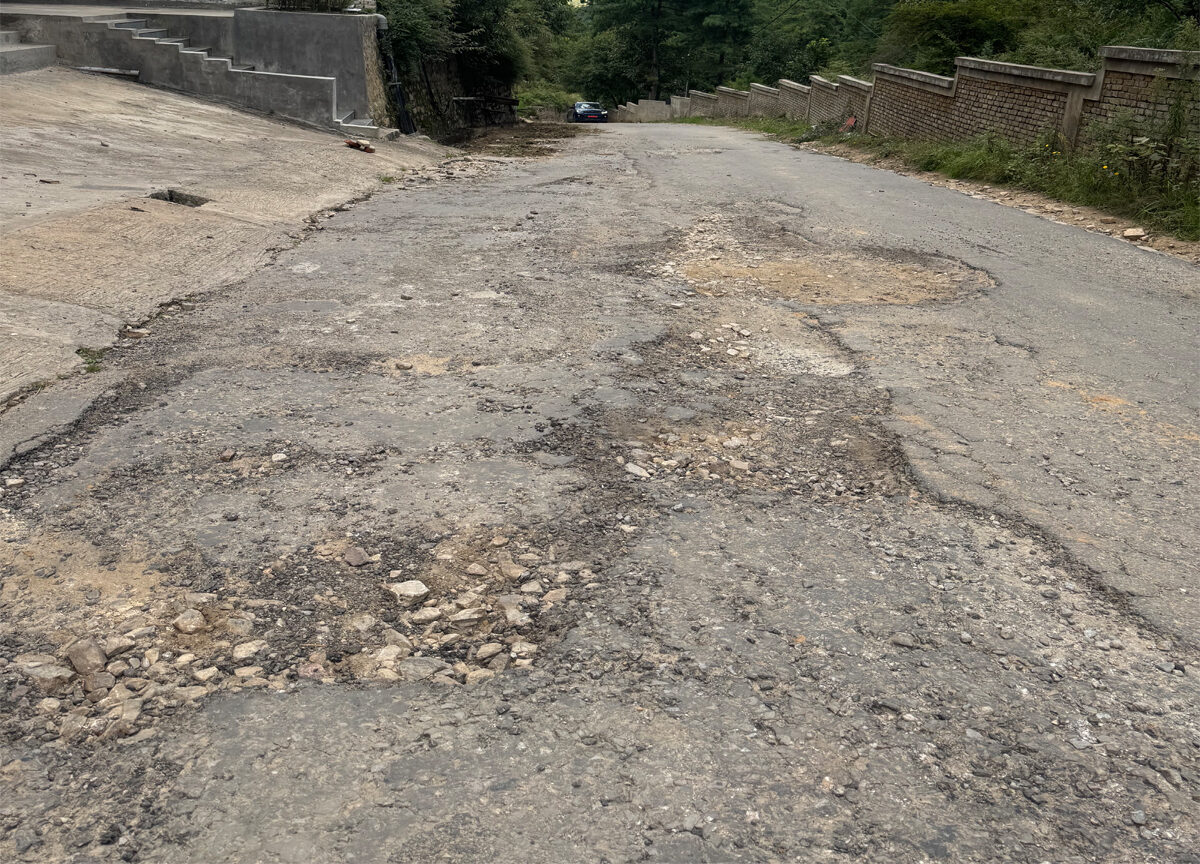 Severely damaged road filled with numerous potholes, making travel difficult.