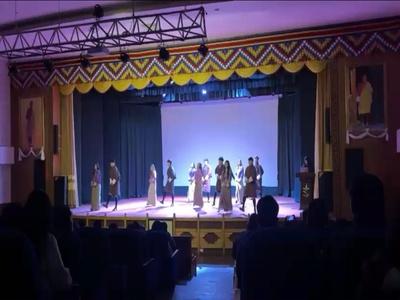 Students performing a group dance on a stage illuminated by green lights during the Communication Arts and Creative Media welcome programme.